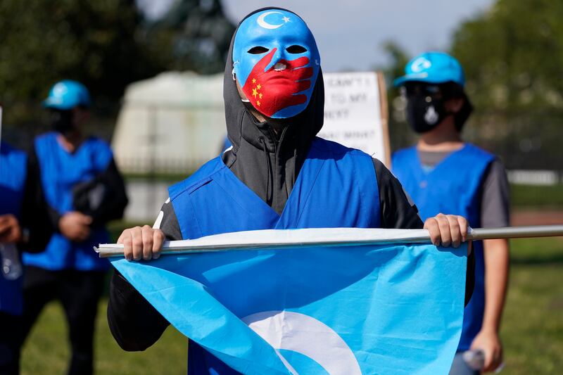 A man wears a mask to protect members of his family who he says have been put into forced labor camps in China, as members of the Uyghur American Association rally in front of the White House, Oct. 1, 2020.