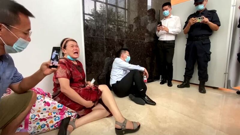 2021年9月13日,恒大位于深圳的总部遭到投资民众的抗议围堵,恒大财富总经理杜亮(左三)被民众围堵坐地睡觉。(路透社视频截图)